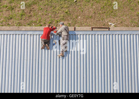 Szczecin, Pologne - 07 Avril 2016 : Les travailleurs de la réparation d'un store toiture en feuilles de métal ondulé, photo prise d'en haut. Banque D'Images