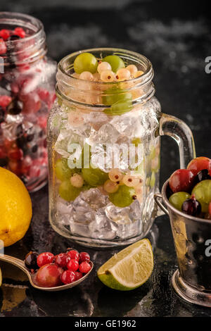 Les baies fraîches avec de la glace en pot Mason sur fond sombre. Régime alimentaire de désintoxication. Banque D'Images