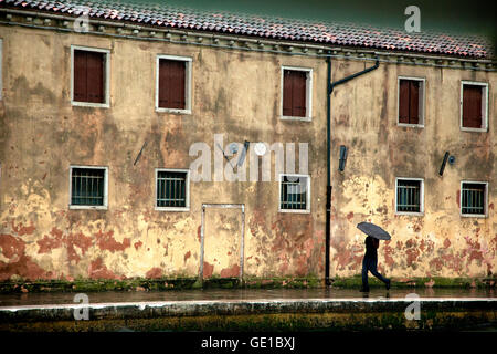 Un homme portant un parapluie et promenades le long du bâtiment en terre cuite à Venise, Italie Banque D'Images