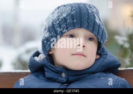 Portrait d'un garçon assis sur un banc dans la neige Banque D'Images