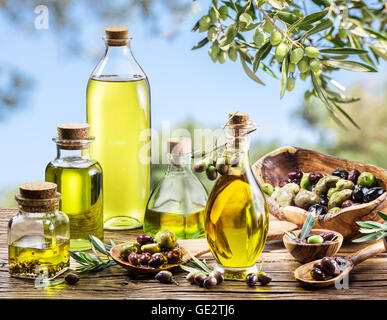 Bouteilles d'huile d'olive sur la vieille table de bois en vertu de l'olivier. Ciel bleu sur l'arrière-plan. Banque D'Images