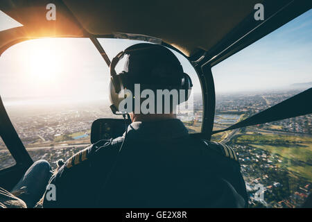 Vue arrière d'un homme pilote aux commandes d'un hélicoptère aux beaux jours. Banque D'Images