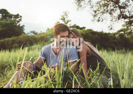 Coup de jeune homme et femme assis ensemble à l'extérieur sur pelouse. Jeune couple romantique dans la prairie. Banque D'Images