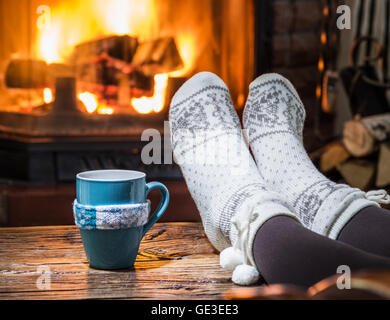 Réchauffement climatique et se reposer près de cheminée. Femme pieds près de la tasse de boisson chaude en face du feu. Banque D'Images