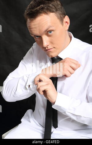 Beau jeune homme dans une chemise blanche sur un fond noir. Banque D'Images