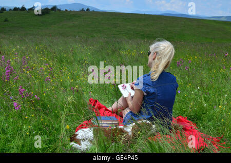 Femme avec un chien est assis sur un pré entouré de fleurs roses et d'écrire quelque chose dans son calepin Banque D'Images