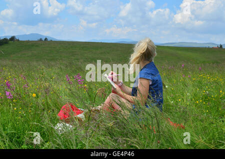 Femme avec un chien est assis sur un pré entouré de fleurs roses et d'écrire quelque chose dans son calepin Banque D'Images