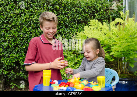 Fillette de trois ans et dix ans, frère et sœur, jouer avec Play-Doh pâte de modélisation. UK. À l'extérieur dans le jardin. Banque D'Images