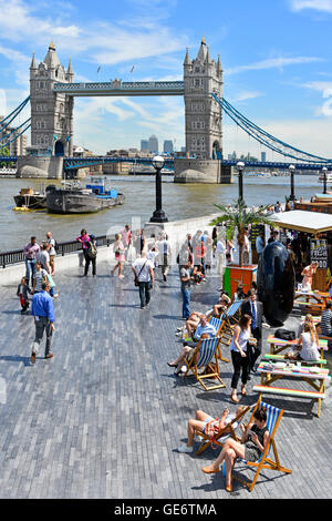 Les touristes et les employés de bureau à l'heure du déjeuner des stands de nourriture rapide mis en place en été, des collations en plein air dans des transats au bord de la Tamise avec le Tower Bridge UK Banque D'Images