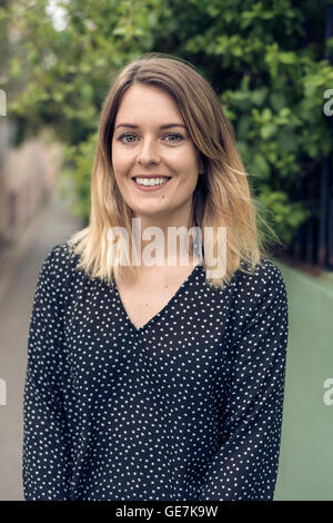 Portrait de profil d'une jeune femme de la rue de verdure derrière elle en souriant Banque D'Images