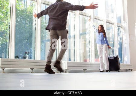 Happy young woman with luggage forme à son petit ami. Homme qui court avec les bras tendus vers la partenaire féminine à l'aéroport. Sh Banque D'Images