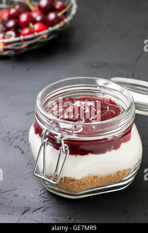 Pas de gâteau au fromage au four dans un bocal en verre avec cerises sur fond noir béton Banque D'Images