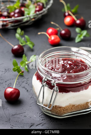 Pas de gâteau au fromage au four dans un bocal en verre avec cerises sur fond noir béton. selective focus Banque D'Images