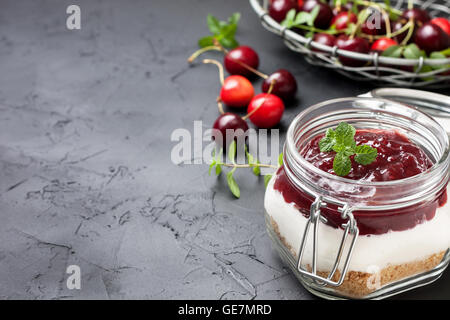 Pas de gâteau au fromage au four dans un bocal en verre avec cerises sur fond noir béton Banque D'Images