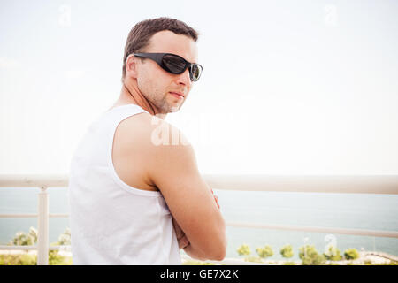 Young Caucasian man en chemise blanche et lunettes noires. Portrait d'été en plein air avec vue mer sur un arrière-plan Banque D'Images