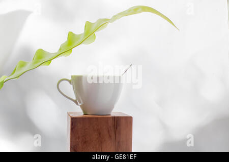 Café tasse blanche avec des petites feuilles vertes sur fond lumineux isolés table top Banque D'Images