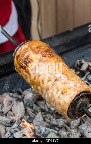 Une femme hongroise qui cuit un Kürtőskalács ou un kürtős kalács sur un feu de charbon de bois dans un salon alimentaire à Budapest, Hongrie. A kürtős Banque D'Images