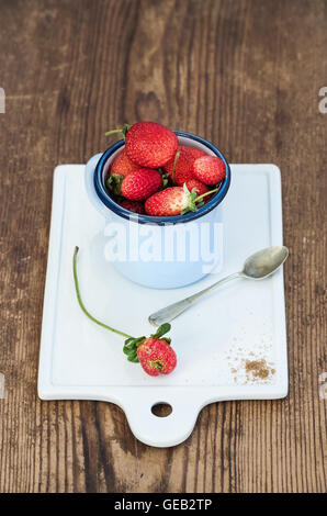 Fresh Fruits rouges fraises en émail bleu mug en céramique blanche sur fond de bois rustique au conseil Banque D'Images