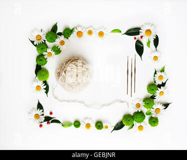Pelote de laine à tricoter et crochets à décor de fleurs de chrysanthèmes et de ficus feuilles sur fond blanc. Vue de dessus. F Banque D'Images