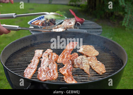 Grill avec des tranches de porc et de la viande, une table avec une assiette de saucisses et de côtes. Banque D'Images