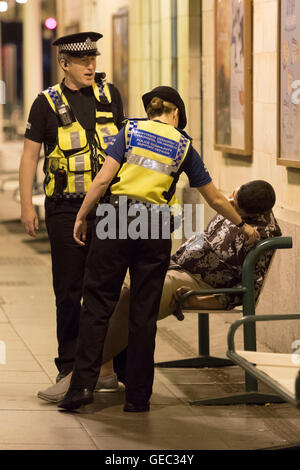 CARDIFF, WALES - 22 juillet : La police britannique des transports aider un homme endormi sur un banc sur la plate-forme lors d'une patrouille à Cardiff Centr Banque D'Images