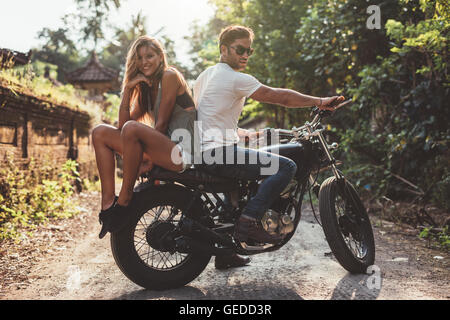 Beau jeune couple sur une moto. Jeune homme et femme sur la moto dans un village. Banque D'Images