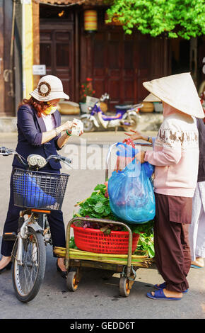 Hoi An, Vietnam - 17 Février 2016 : acheteur asiatique et commerçant d'une chapeau traditionnel vietnamien vert frais de vente dans les épinards de la rue du marché à Hoi An, au Vietnam. Banque D'Images