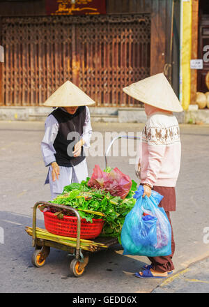 Hoi An, Vietnam - 17 Février 2016 : acheteur asiatique et commerçant d'une hat vietnamiens traditionnels épinards frais de vente dans le marché de rue à Hoi An, au Vietnam. Banque D'Images