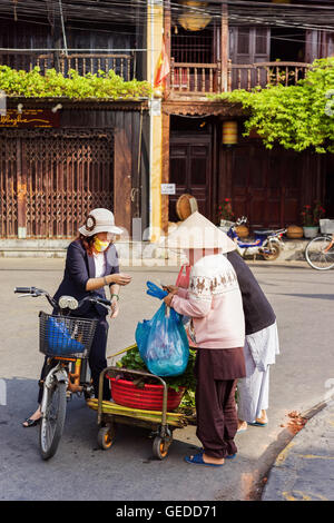 Hoi An, Vietnam - 17 Février 2016 : acheteur asiatique et commerçant d'une vietnamienne traditionnelle hat vendre vert épinards dans la rue market à Hoi An, au Vietnam. Banque D'Images