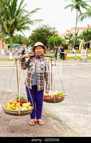 Hoi An, Vietnam - 16 Février 2016 : opérateur accomplissant les fruits dans des bols sur ses épaules dans la rue à Hoi An, au Vietnam. Ramboutans, mangue, banane et mandarin. Banque D'Images