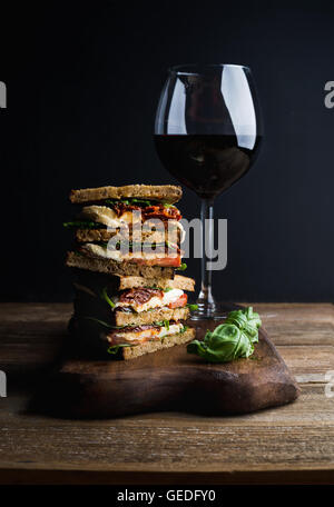 Caprese sandwich ou panini et verre de vin rouge. Le pain de grains entiers, mozzarella, tomates séchées, basilic. Fond sombre, composition verticale Banque D'Images