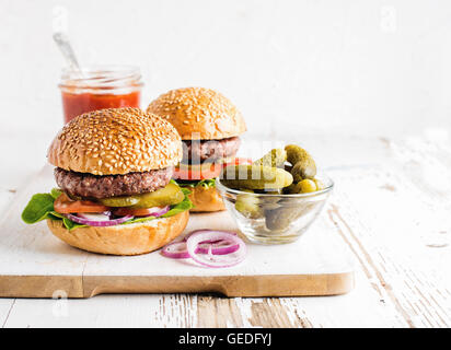 Deux des hamburgers faits maison, des cornichons, du ketchup et des oignons sur du conseil en bois blanc Banque D'Images