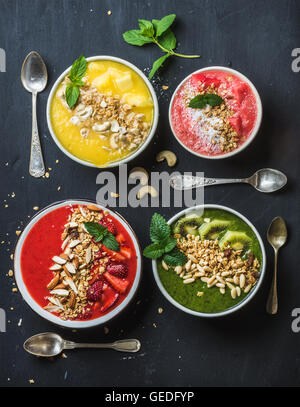 Petit-déjeuner d'été en bonne santé concept. Smoothie aux fruits colorés avec des écrous, des bols de céréales d'avoine et de feuilles de menthe sur fond noir. Jaune, rose, rouge, vert. Vue de dessus, la composition verticale Banque D'Images