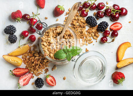 Petit-déjeuner sain ingrédients. Granola avoine dans le jar servi avec des tranches de pêche, de fraise, de cerise douce et les mûres sur la lumière en arrière-plan, Vue de dessus, composition horizontale Banque D'Images