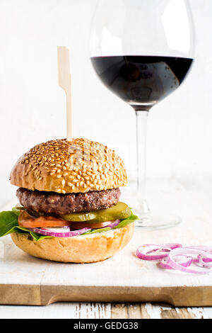 Burger maison en bois blanc sur la carte servant avec oignon, verre de vin rouge. Banque D'Images