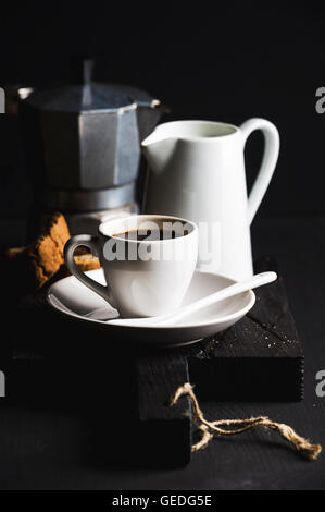 Service à café italienne pour le petit-déjeuner. Tasse d'expresso chaud, crème de lait, cantucci et moka pot sur rustique en bois sombre sur fond noir Banque D'Images