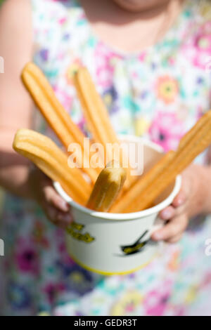 Un gros plan d'une jeune fille dans une jolie robe à fleurs tenant une tasse de papier rempli de churros Banque D'Images