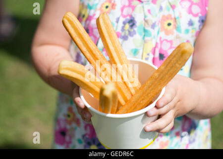 Un gros plan d'une jeune fille dans une jolie robe à fleurs tenant une tasse de papier rempli de churros, beignets frits sticks Banque D'Images