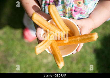 Un gros plan d'une jeune fille dans une jolie robe à fleurs tenant une tasse de papier rempli de churros, beignets frits sticks avec cin Banque D'Images