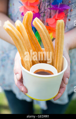 Gros plan d'une femme portant une guirlande de fleurs hawaïennes colorées, tenant une tasse de papier rempli de sweet sugar coated churros avec Banque D'Images