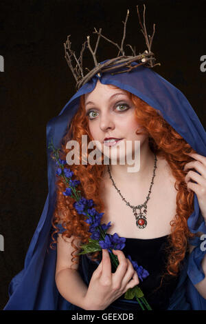 Belle jeune femme aux cheveux rouges portant robe bleue en velours et couronne de rameaux Banque D'Images