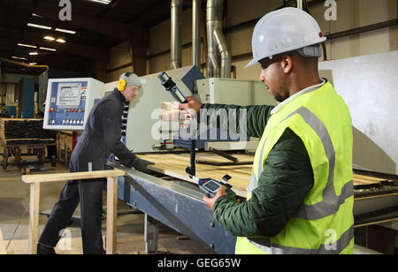 Un ingénieur de l'environnement surveille les niveaux de poussière à côté d'une machine de coupe de bois dans une usine de fabrication au Royaume-Uni. Banque D'Images