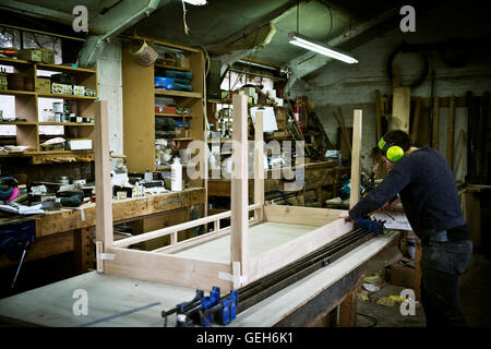 Un homme travaillant dans l'atelier d'un fabricant de meubles, l'assemblage d'un tableau. Banque D'Images