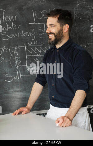 Baker, debout devant un tableau avec une recette du pain d'inscrit. Banque D'Images