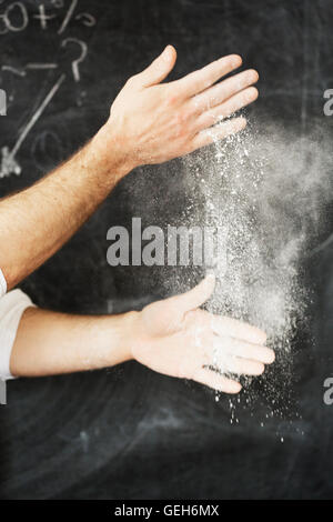 Close up of a baker, debout devant un tableau noir, en époussetant ses mains avec de la farine. Banque D'Images