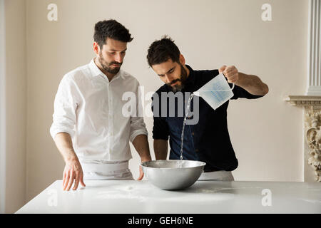 Deux boulangers debout à une table, la préparation de pâte à pain, verser de l'eau à partir d'une éprouvette graduée dans un bol en métal. Banque D'Images