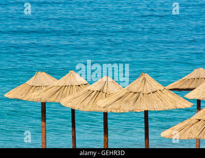 Les parasols de paille sur la plage aux eaux turquoises dans l'arrière-plan Banque D'Images