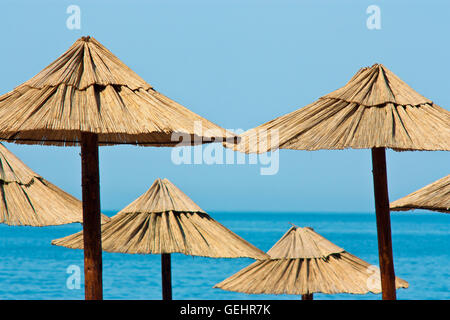 Les parasols de paille sur la plage aux eaux turquoises et bleu ciel à l'arrière-plan Banque D'Images