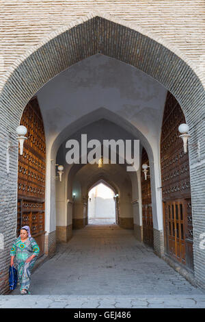 Femme ouzbek dans sa robe traditionnelle promenades à travers le passage voûté à Boukhara, Ouzbékistan. Banque D'Images