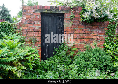 Une porte en bois fermée situé dans un mur de brique rouge dans un jardin luxuriant. Banque D'Images